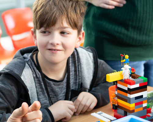 A boy building a lego tower and smiling