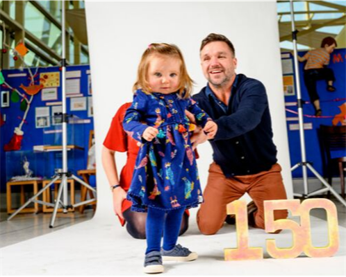 Evie Cox in a blue dress with her parents and a sign that says 150
