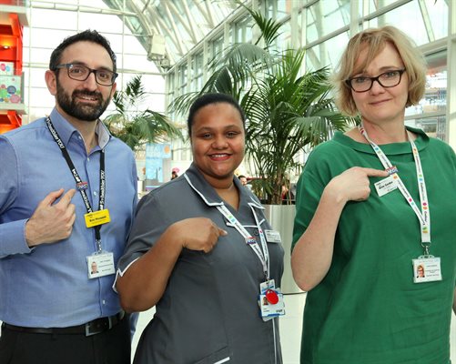 Three Evelina London staff pointing to NHS rainbow badges they are wearing