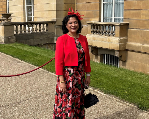 Dr Bidisha Lahoti in a red floral dress and red jacket smiling at the camera at the royal garden party