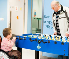 Boy in wheelchair playing table football with grandparent