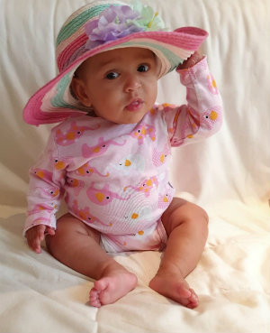 One-year-old Sayanna wearing a pink outfit and a colourful hat.