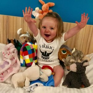 Evie Cox smiling with her hands up in the air and lots of toys.