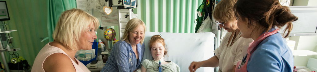 Teenage girl in bed surrounded by family, friends and staff