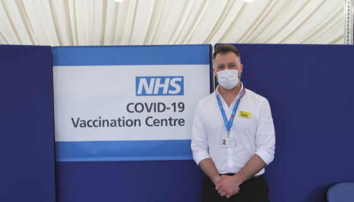 Vaccinator Chris with a sign that says COVID-19 Vaccination Centre.