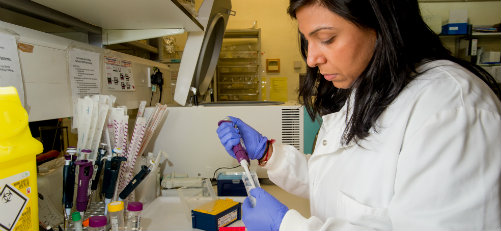 A researcher in a laboratory with test tubes and other scientific equipment.